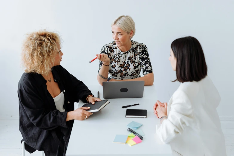 two women sitting at a table talking to each other, pexels contest winner, three women, sitting in office, with a white background, upper body image