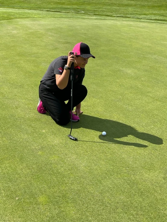 a man kneeling on top of a green field next to a golf ball, lighting her with a rim light, in the sun, reflection of iphone in visor, profile image