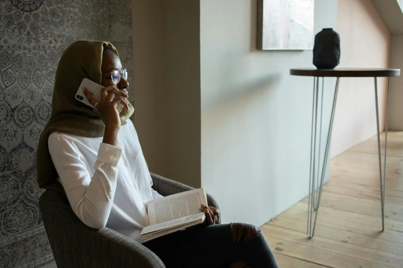 a woman sitting in a chair talking on a cell phone, trending on pexels, hurufiyya, wearing a head scarf, reading nook, integrated synthetic android, ashteroth