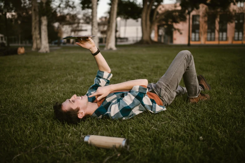 a man laying on top of a lush green field, by Carey Morris, pexels contest winner, happening, holding a book, casual game, hold up smartphone, sydney hanson
