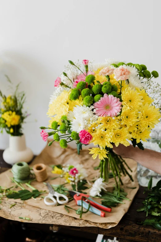 a person holding a bunch of flowers on a table, creating a soft, pink and yellow, stunning design, commercially ready