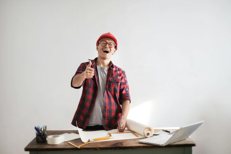 a man standing in front of a desk with a laptop, by Jang Seung-eop, pexels contest winner, wearing a red lumberjack shirt, being delighted and cheerful, architectural planning, as well as the handyboy