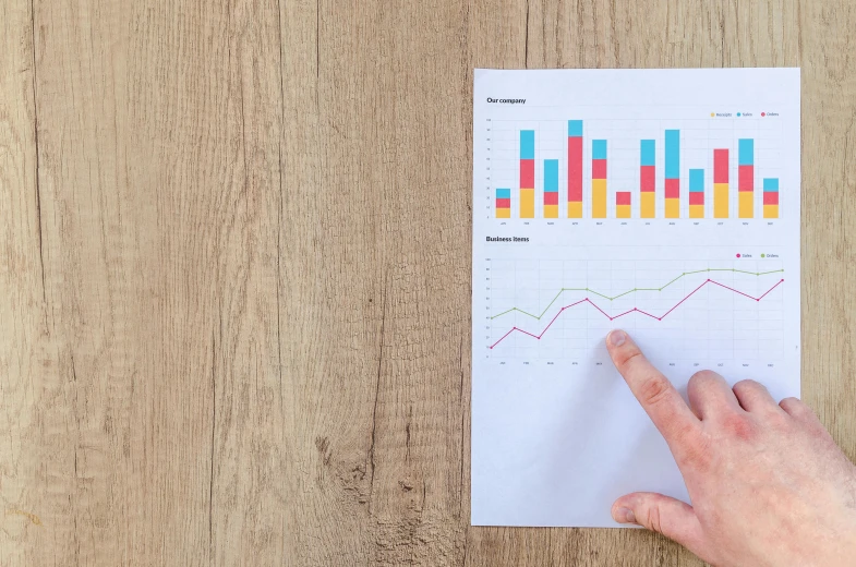 a person pointing at a graph on a piece of paper, by Emma Andijewska, trending on unsplash, on a wooden desk, 🦩🪐🐞👩🏻🦳, bar charts, cover shot