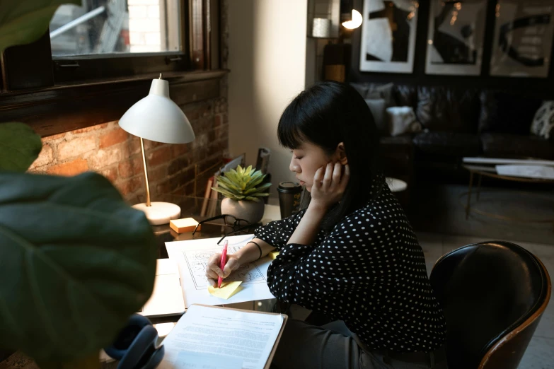 a woman sitting at a table writing on a piece of paper, pexels contest winner, gemma chen, home office, lit from the side, well drawn