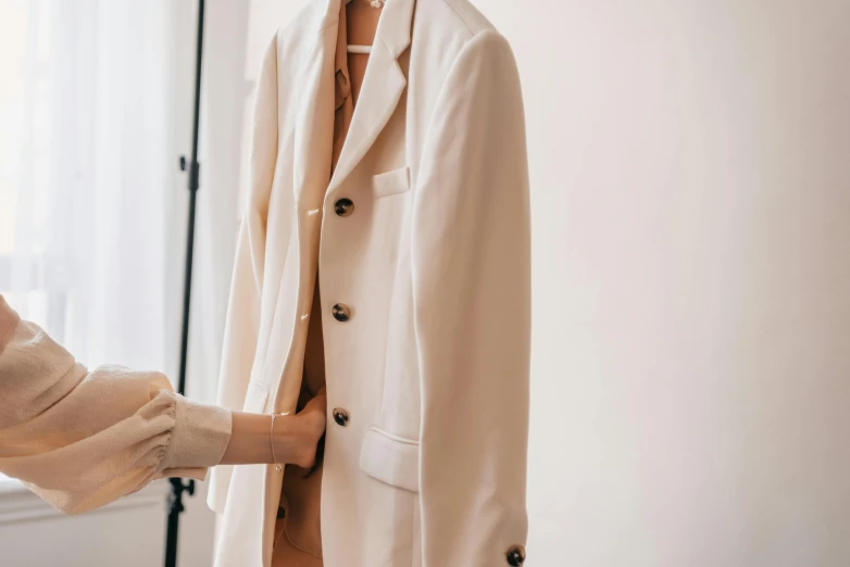 a woman standing next to a mannequin in a room, trending on pexels, light brown trenchcoat, wearing a white tuxedo, exiting from a wardrobe, zoomed in