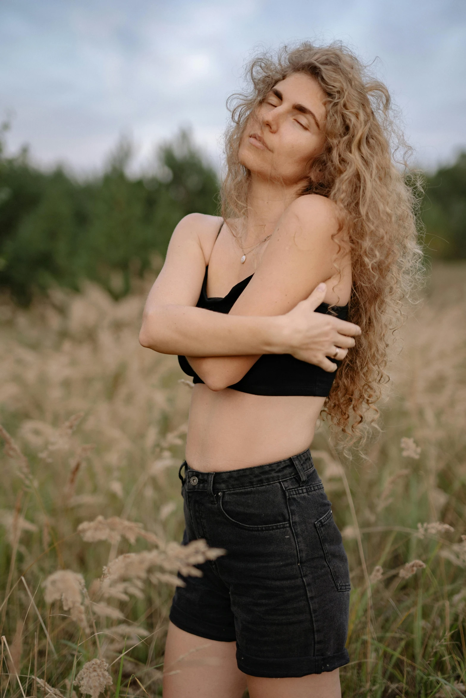a woman standing in a field of tall grass, by Attila Meszlenyi, trending on pexels, renaissance, wearing bra, curly blond, wearing a black shirt, belly button showing
