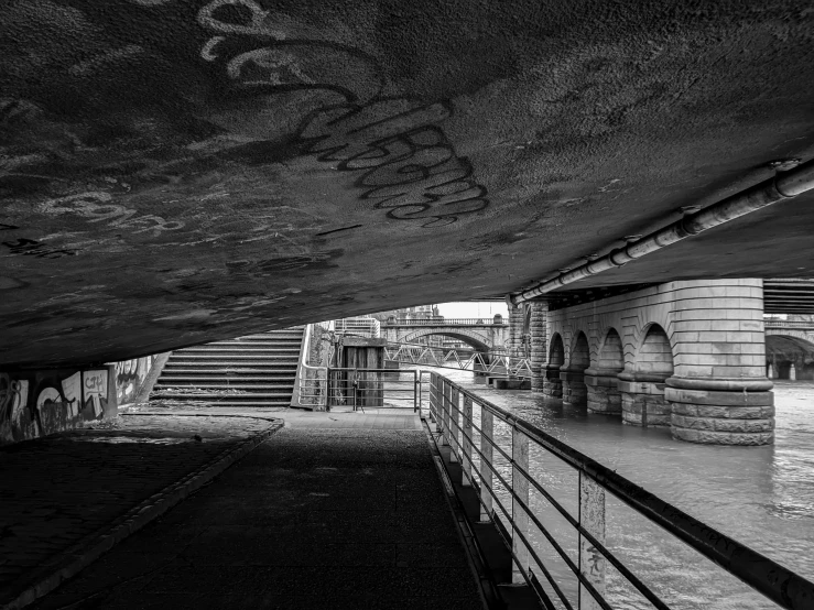 a black and white photo of a bridge, by Raphaël Collin, graffiti, london south bank, stairs and arches, hdr photograph, hiding