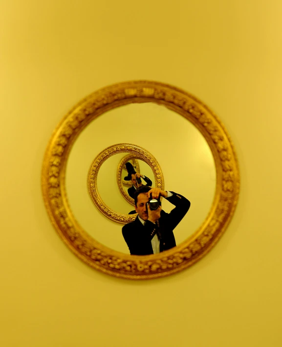 a person taking a picture of themselves in a mirror, an album cover, unsplash, surrealism, ((yellow magic orchestra)), 3 0 0 mm, gold framed, monocle