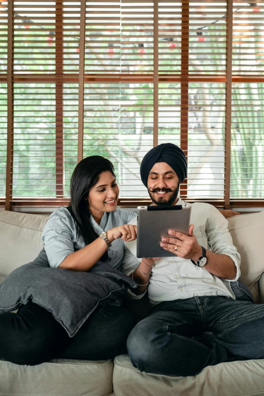 a man and woman sitting on a couch looking at a tablet, inspired by Manjit Bawa, pexels contest winner, turban, proud looking, australian, malaysian