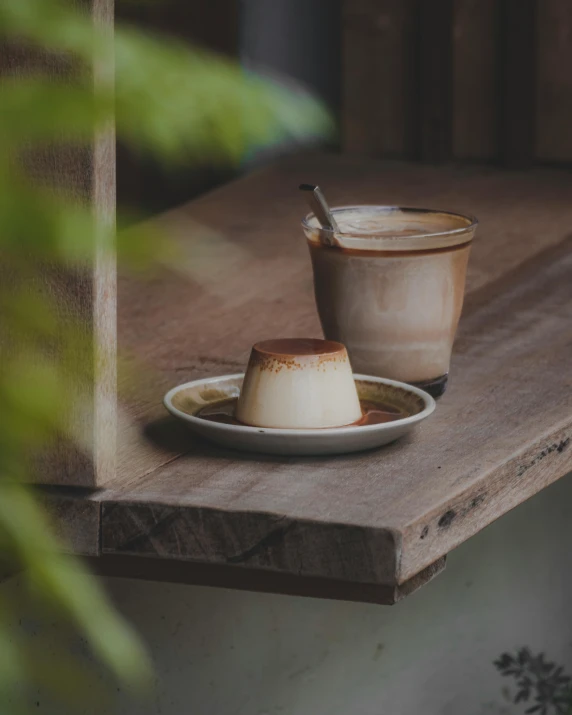 a white plate topped with a dessert next to a cup of coffee, unsplash, australian tonalism, flan, wooden platforms, background image, pots with plants