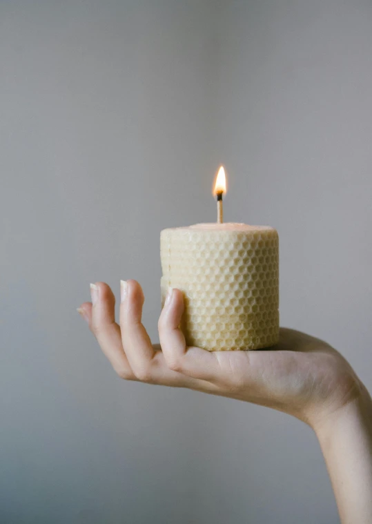 a person holding a candle in their hand, honeycomb, textured base ; product photos, small, image