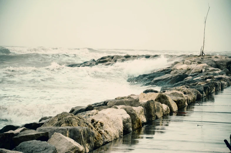 a man standing on top of a rock wall next to the ocean, inspired by Elsa Bleda, unsplash, romanticism, rushing water, ignant, overexposed photograph, medium format