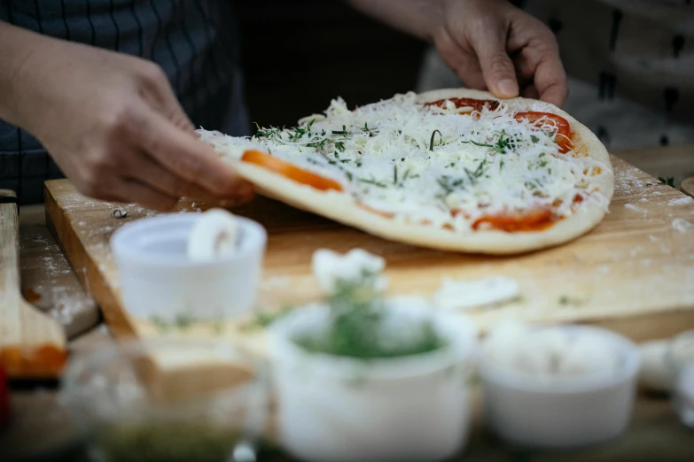 a person making a pizza on a cutting board, by Tom Bonson, unsplash, fan favorite, herbs, lots of mozzarella balls, al fresco