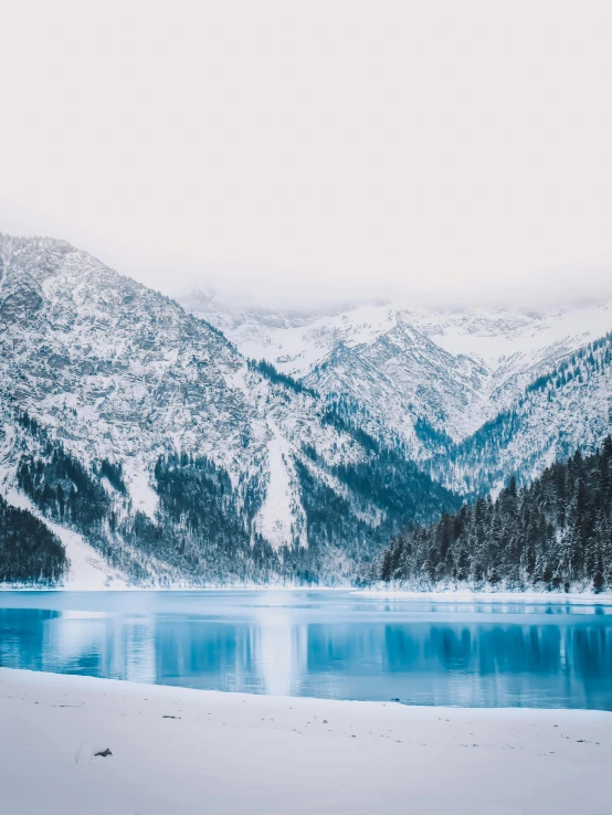 a large body of water surrounded by snow covered mountains, pexels contest winner, winter vibes, blue and gray colors, build in a forest near of a lake, cold as ice! 🧊