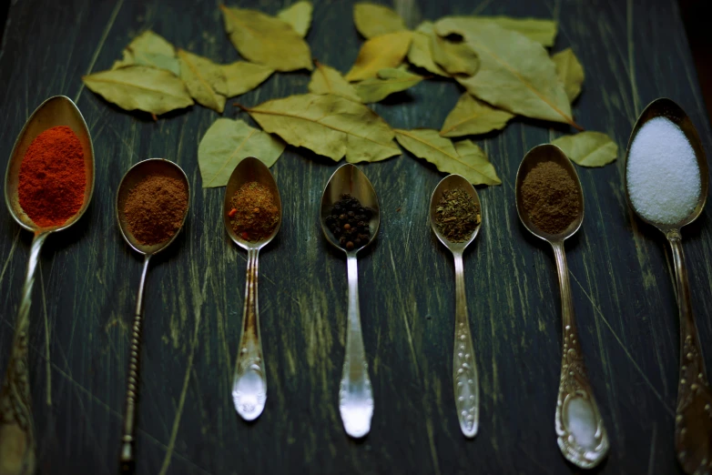 a group of spoons sitting on top of a wooden table, a still life, unsplash, hurufiyya, leaves, spices, photo taken on fujifilm superia, mint