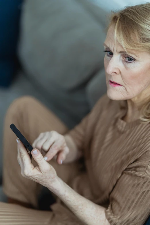 a woman sitting on a couch looking at a cell phone, pexels, dementia, close up of a blonde woman, serious, ad image