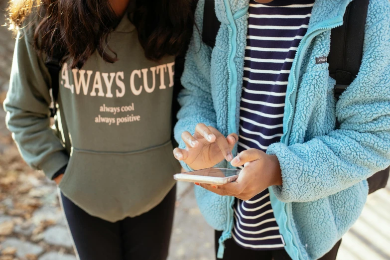 a couple of women standing next to each other, a picture, trending on pexels, wearing sweatshirt, insisted on cutting in line, cell phone, teal aesthetic