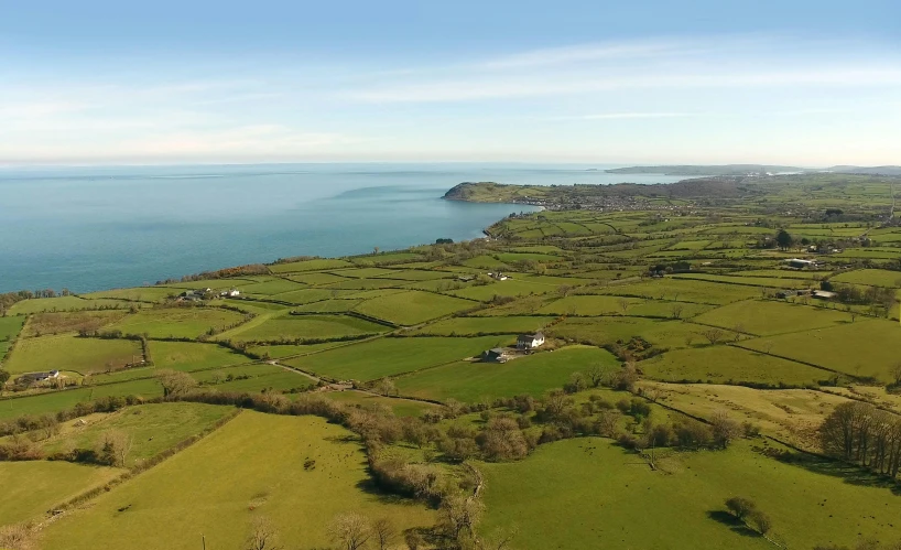 a large body of water next to a lush green field, by Julian Allen, pembrokeshire, aerial, views to the ocean, sunny sky