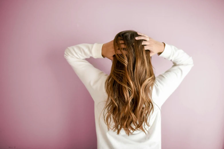 a woman with long brown hair standing in front of a pink wall, trending on pexels, hands in her hair. side-view, bedhead, seen from the back, a blond