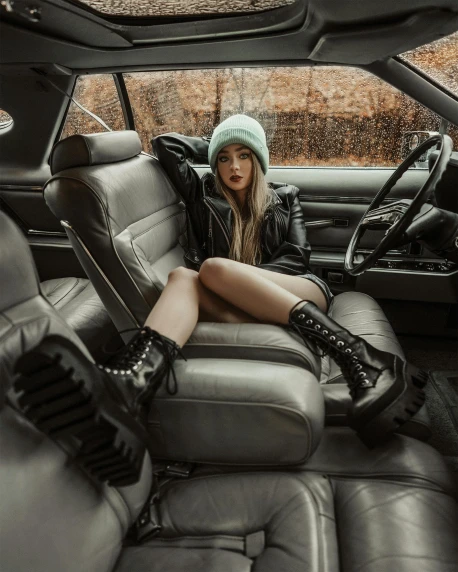 a woman sitting in the back seat of a car, inspired by Elsa Bleda, trending on pexels, wearing tall combat boots, latex domme, she is wearing a hat, sydney sweeney