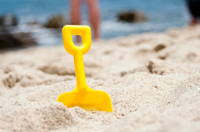 a yellow shovel sitting on top of a sandy beach, playing, hansa yellow, subtle detailing, bright colour