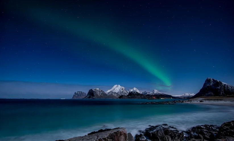a body of water with a mountain in the background, by Ejnar Nielsen, pexels contest winner, romanticism, blue and green light, the night sky is a sea, winter, coastal