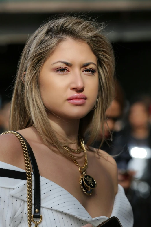 a woman in a white top holding a cell phone, by Robbie Trevino, trending on pexels, photorealism, glamorous runway model, sad look, wearing gold chain, closeup - view