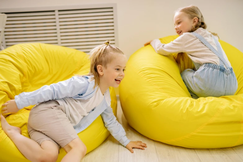two young girls sitting on bean bags in a room, pexels contest winner, yellow scheme, straya, bouncy belly, casual game