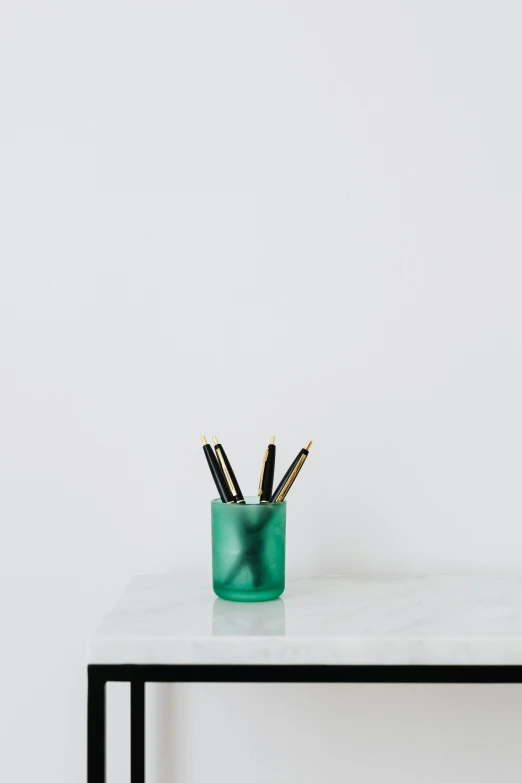 a green vase sitting on top of a white table, by Nicolette Macnamara, featured on unsplash, holding pencil, small rectangular glasses, cyan fog, miniature product photo