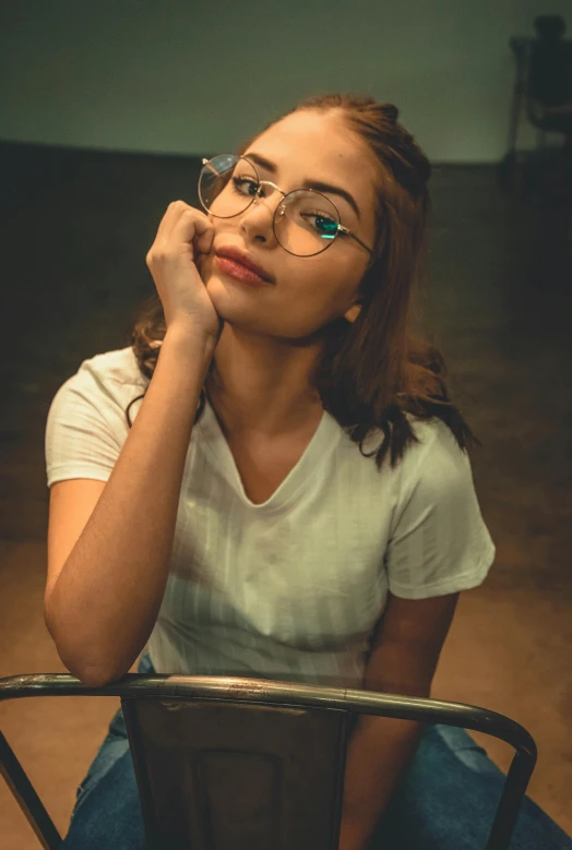 a woman with glasses sitting on a chair, a colorized photo, inspired by Elsa Bleda, trending on pexels, photorealism, isabela moner, handsome girl, square rimmed glasses, dressed in a white t shirt