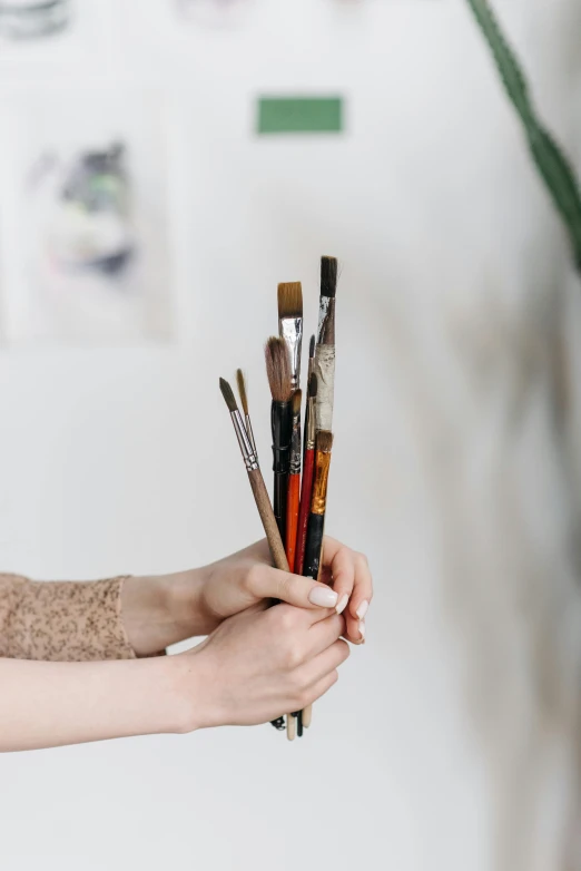 a woman holding a bunch of paint brushes, a photorealistic painting, trending on pexels, brown, but minimalist, instagram photo, studio photograph