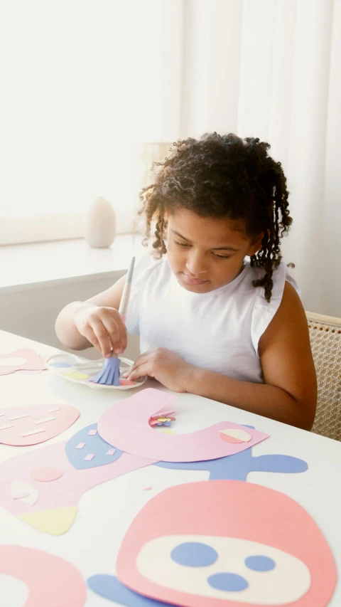 a little girl that is sitting at a table, paper cutouts of plain colors, crafting, thumbnail, low quality photo