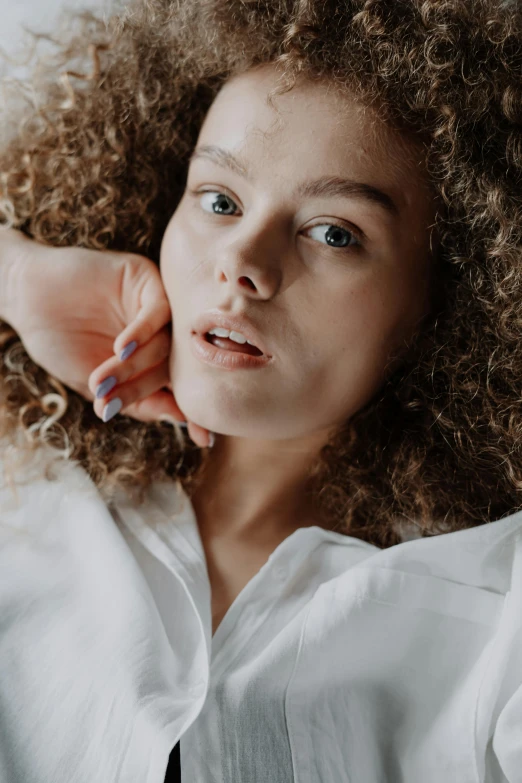 a woman with curly hair wearing a white shirt, trending on pexels, androgyn beauty, zoomed in, relaxed pose, full colour