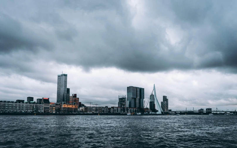 a large body of water with a city in the background, by Jacob Toorenvliet, pexels contest winner, hypermodernism, stormy clouds outdoor, the netherlands, the photo was taken from a boat, overcast gray skies