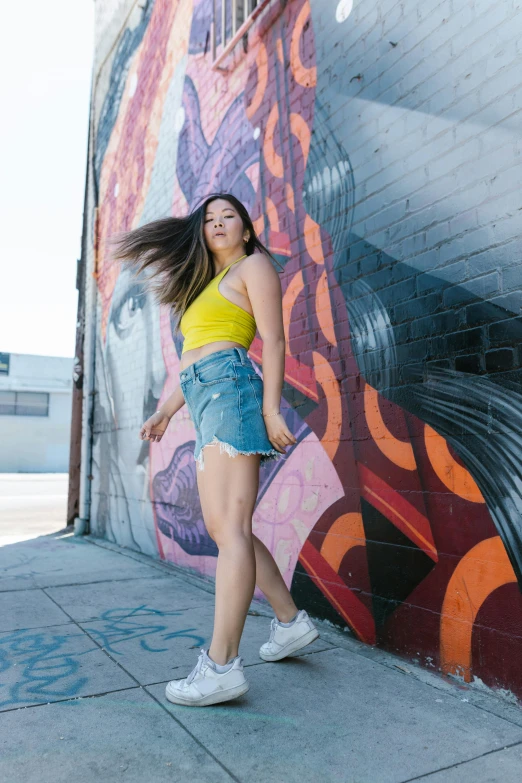 a woman standing in front of a graffiti wall, by Briana Mora, wearing yellow croptop, asian girl with long hair, promo image, los angeles ca