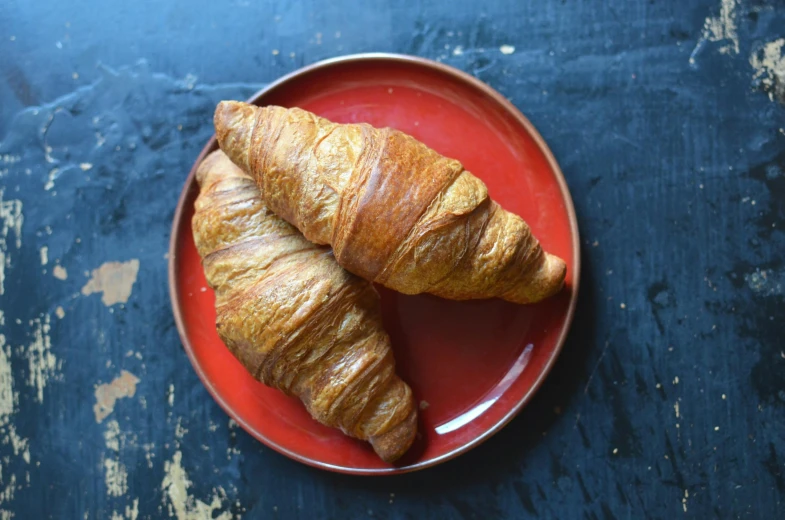 two croissants are on a red plate, a portrait, inspired by Charles Le Roux, unsplash, hurufiyya, woodfired, various sizes, grain”