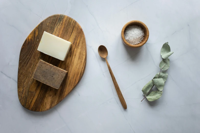 a wooden plate topped with a bar of soap next to a bowl of sea salt and a wooden spoon, a still life, trending on pexels, organic shapes, advert, bog oak, birdseye view