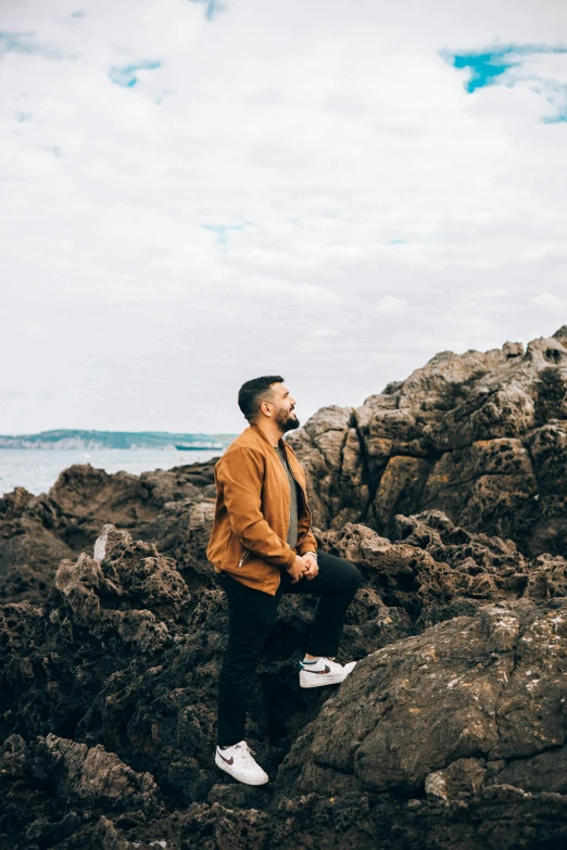 a man sitting on a rock in front of the ocean, rugged beard, kneeling and looking up, lachlan bailey, music