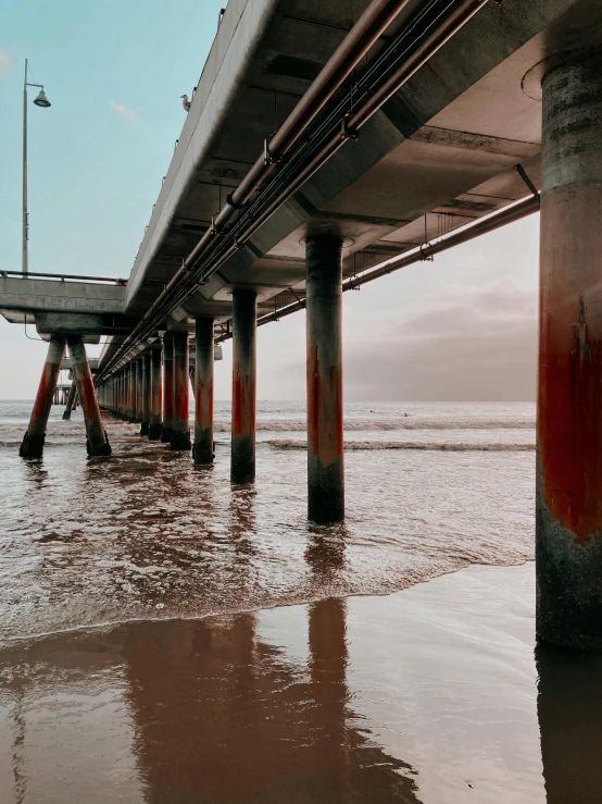 the underside of a bridge over a body of water, a colorized photo, unsplash contest winner, santa monica beach, tall columns, brown water, profile image