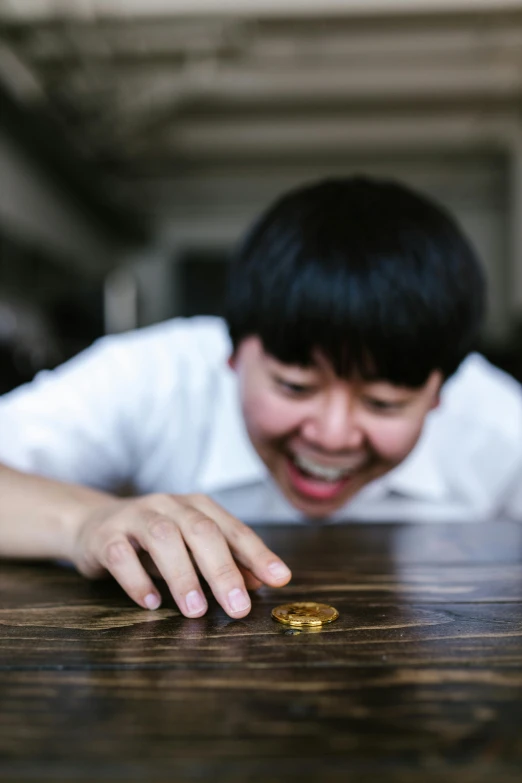 a close up of a person looking at a coin on a table, by Jang Seung-eop, giggling, thrown tables, gold, smol