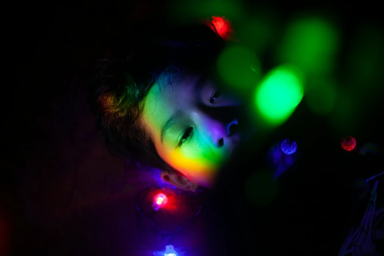 a little boy that is laying down in the dark, inspired by Elsa Bleda, pexels, light and space, colored lasers, hanging out with orbs, close-up photograph, multi - coloured