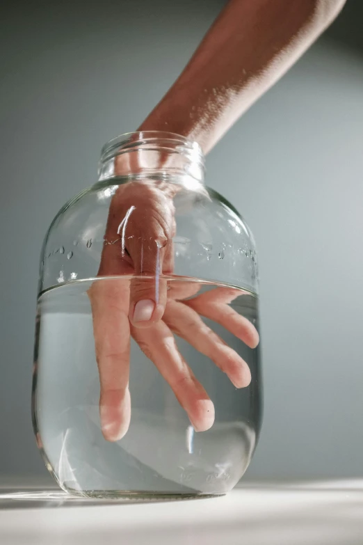 a close up of a person's hand in a jar of water, by Marina Abramović, unsplash, hyperrealism, waving, ignant, concept photo, large tall