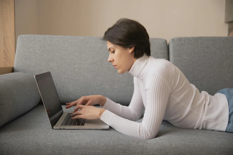 a woman laying on a couch using a laptop, trending on pexels, wearing a white sweater, bent - over posture, official screenshot, elegant regal posture