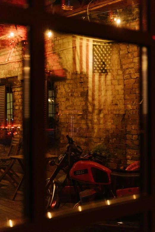 a motorcycle parked in front of a brick building, american flags, candlelit restaurant table, seen through a window, red flags