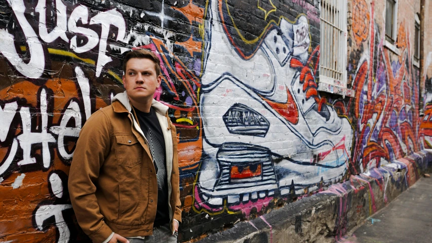 a man standing in front of a graffiti covered wall, inspired by Seb McKinnon, browny, sneaker, james gleeson, tv still