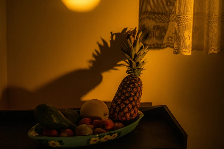 a pineapple sitting on top of a table next to a bowl of fruit, inspired by Elsa Bleda, shadow play, under light, lit from the side, indoor light