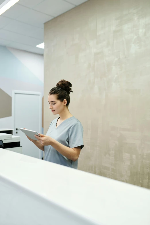 a woman standing in front of a counter holding a tablet, by Arabella Rankin, unsplash, happening, medical complex, grey, brown, looking around a corner