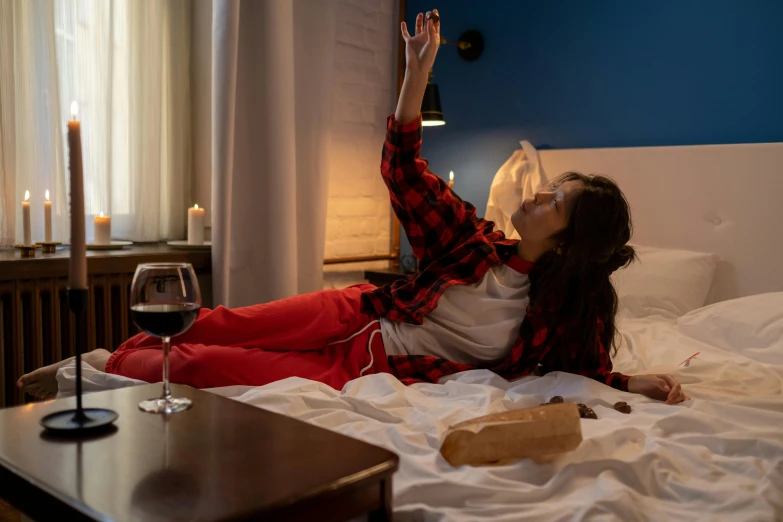 a woman laying on a bed with a glass of wine, pexels contest winner, red shirt brown pants, holding up a night lamp, hungover, arms stretched out