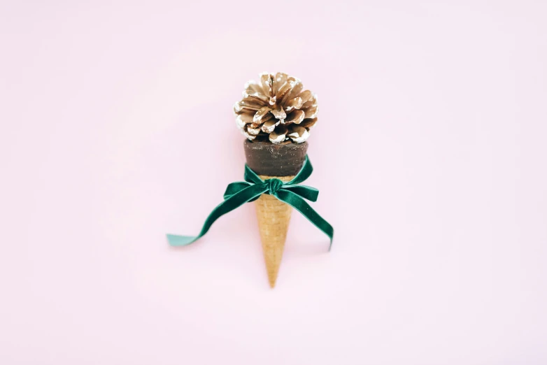 a pine cone with a ribbon wrapped around it, by Emma Andijewska, pexels contest winner, magic realism, ice cream, plain background, gold and green, miniature product photo