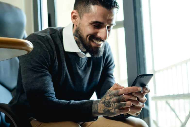 a man sitting in a chair looking at his cell phone, trending on pexels, photograph of a sleeve tattoo, smug smile, professional profile picture, raphael lecoste